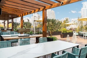 Un espace de restauration en plein air agrémenté de pergolas en bois, de chaises vertes et de tables.