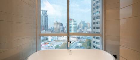 A modern bathroom with a large bathtub, a window with a city view, and tiled walls.