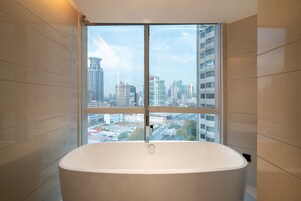 A modern bathroom with a large bathtub, a window with a city view, and tiled walls.