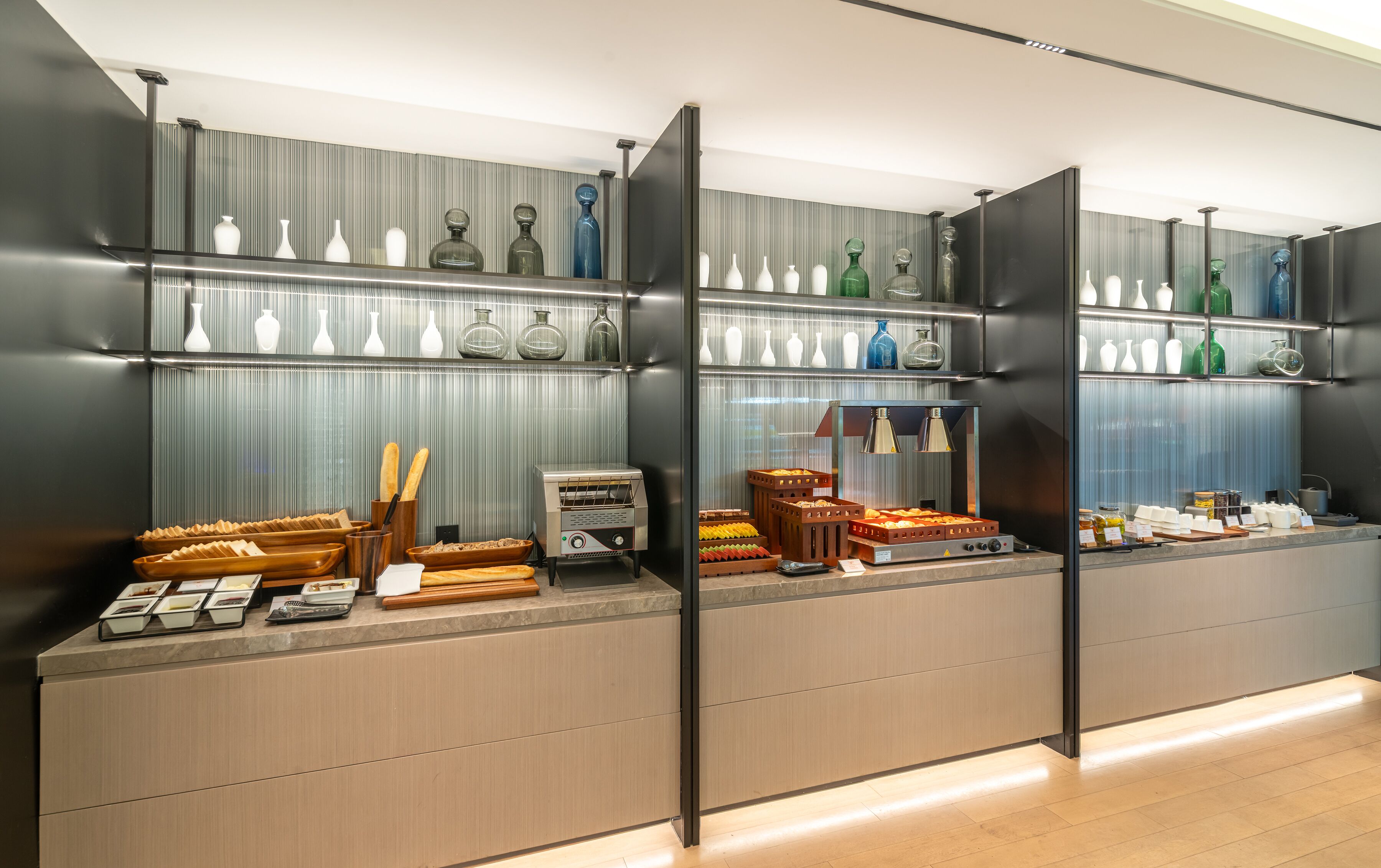 A modern kitchen with wooden cabinets, a countertop with bread, and shelves with glassware.