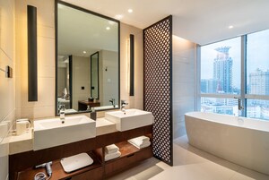 A modern bathroom with two sinks, a large mirror, a bathtub, and a city view.