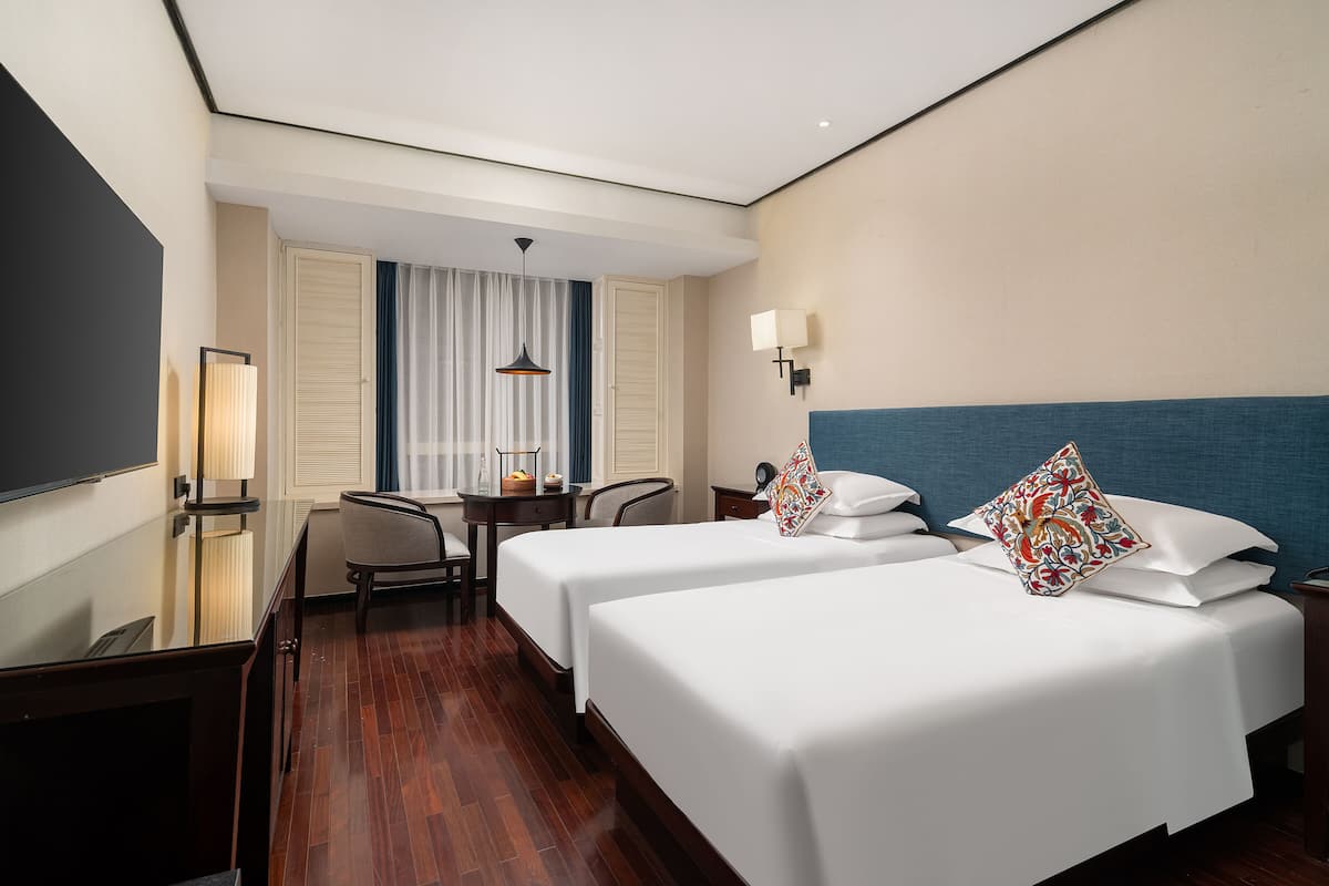 Een hotelkamer met twee bedden, een bureau, een stoel, een televisie en een raam met gordijnen.