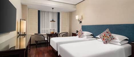 A hotel room with two beds, a desk, a chair, a TV, and a window with curtains.