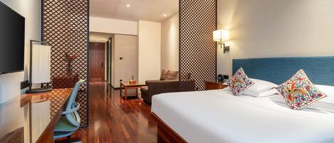 A hotel room with a large bed, a desk, a chair, and a wooden floor.