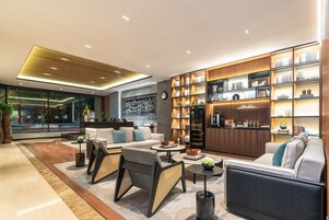 A modern living room with a sofa, armchairs, and a coffee table. There is a bookshelf with decorative items and a clock on the wall.