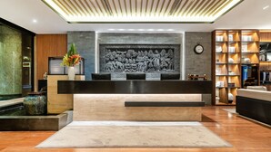 Un espace d’accueil au design moderne, comprenant un comptoir de réception, un mur décoratif orné d’une sculpture en relief, une horloge et un intérieur bien éclairé.