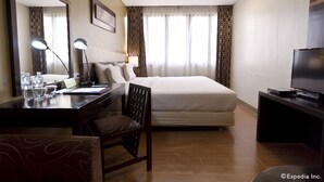 Une chambre d’hôtel comprenant un lit, un bureau avec une lampe, une chaise, un téléviseur et un grand miroir.
