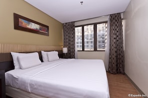 A hotel room with a large bed, a headboard, a wall-mounted painting, patterned curtains, and a window with a view of buildings. - Summit Circle Cebu (Cebu City)
