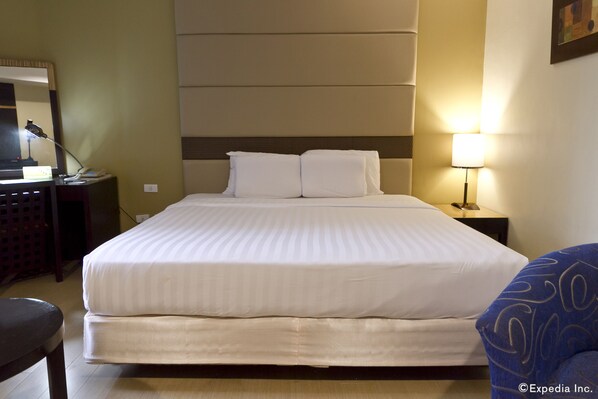 Habitación de hotel con una cama grande, un escritorio con lámpara, una silla y una mesita de noche.