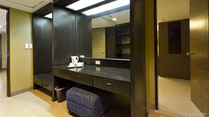 Une chambre d’hôtel de taille modeste, avec un bureau de couleur sombre, un grand miroir et un petit tabouret.