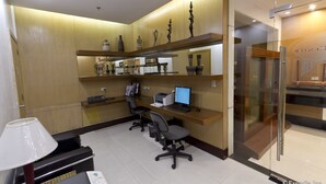 Un espace d’accueil comprenant un ordinateur, des chaises et un bureau. On y trouve également des étagères avec des objets décoratifs et une porte en verre.