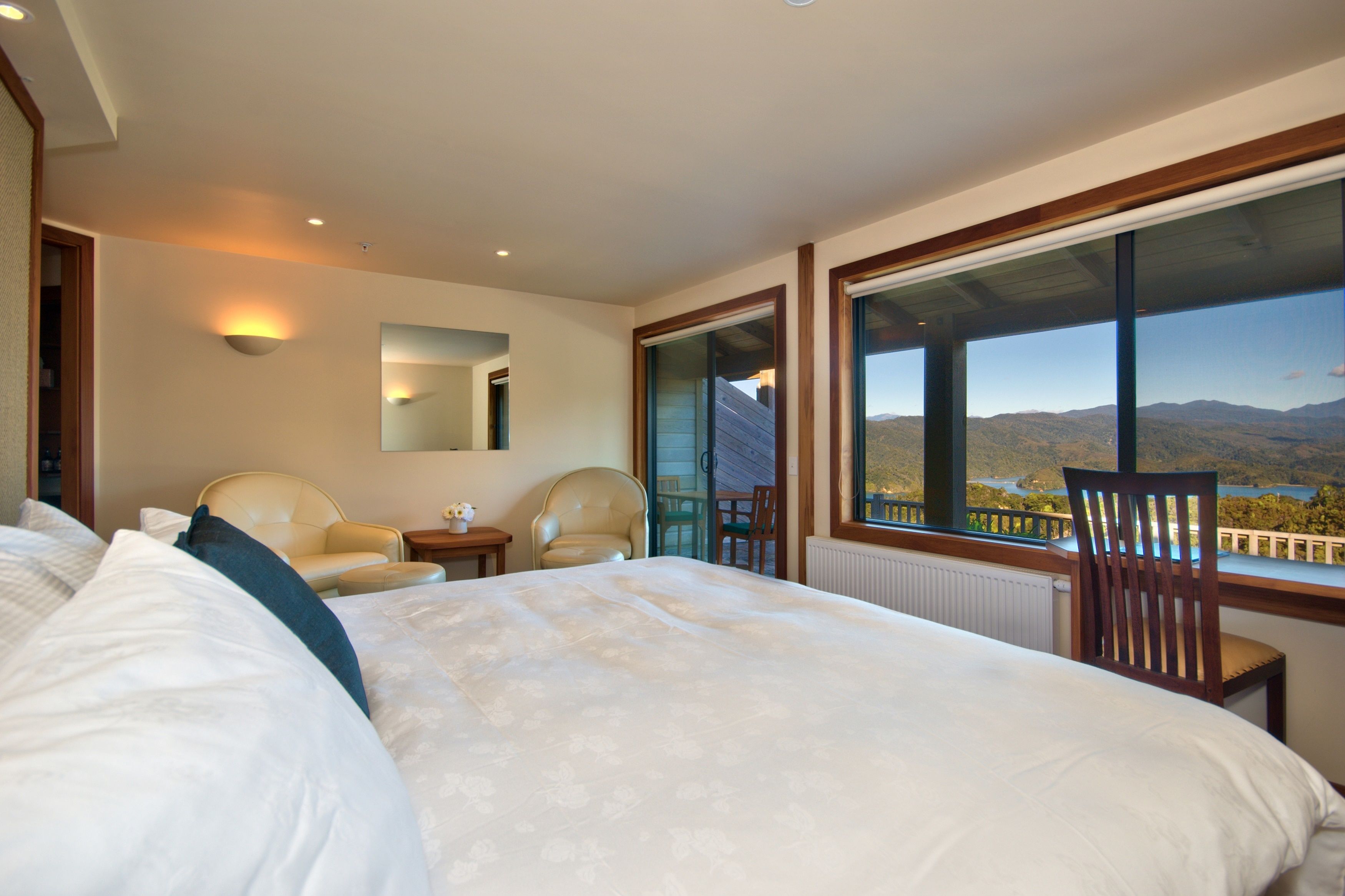 Ein Hotelzimmer mit einem großen Bett, zwei Stühlen, einem kleinen Tisch und Bergblick durch große Fenster.