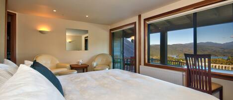 Ein Hotelzimmer mit einem großen Bett, zwei Stühlen, einem kleinen Tisch und Bergblick durch große Fenster.