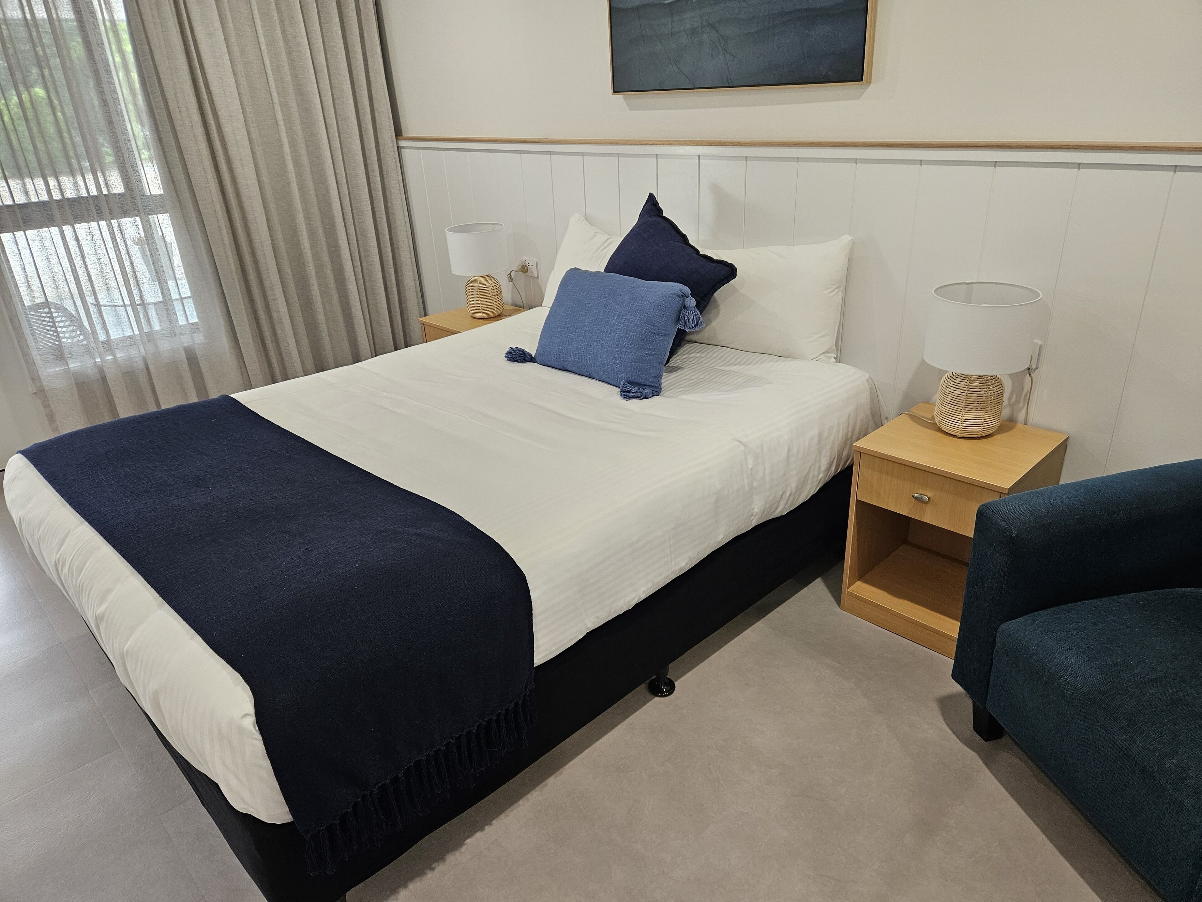 Ein ordentlich eingerichtetes Hotelzimmer mit Bett, Nachttischen, einer Lampe und einem Sessel.