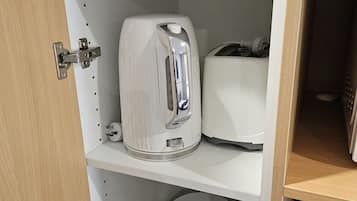Una cocina con tostadora, hervidor y un cajón con bolsitas de té y galletas.