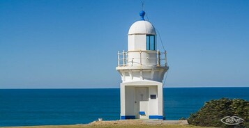 Un faro con una estructura blanca y azul, cielo despejado y el océano al fondo.