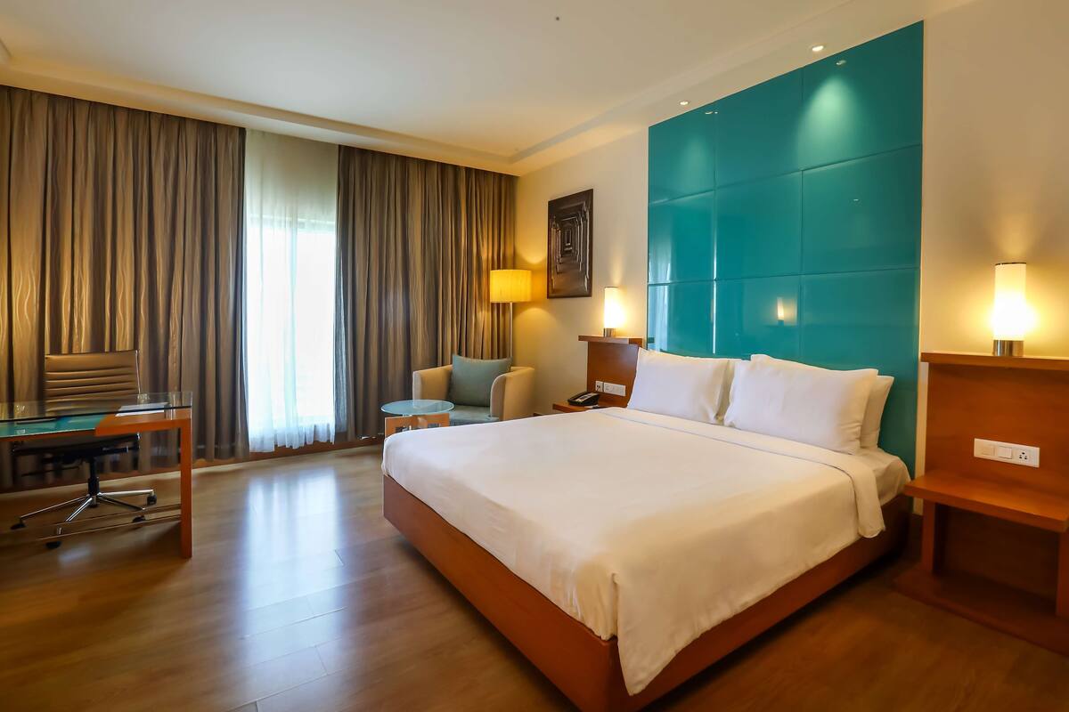 Ein Hotelzimmer mit einem großen Bett, einem Schreibtisch mit Stuhl, einem kleinen runden Tisch und einer Couch.