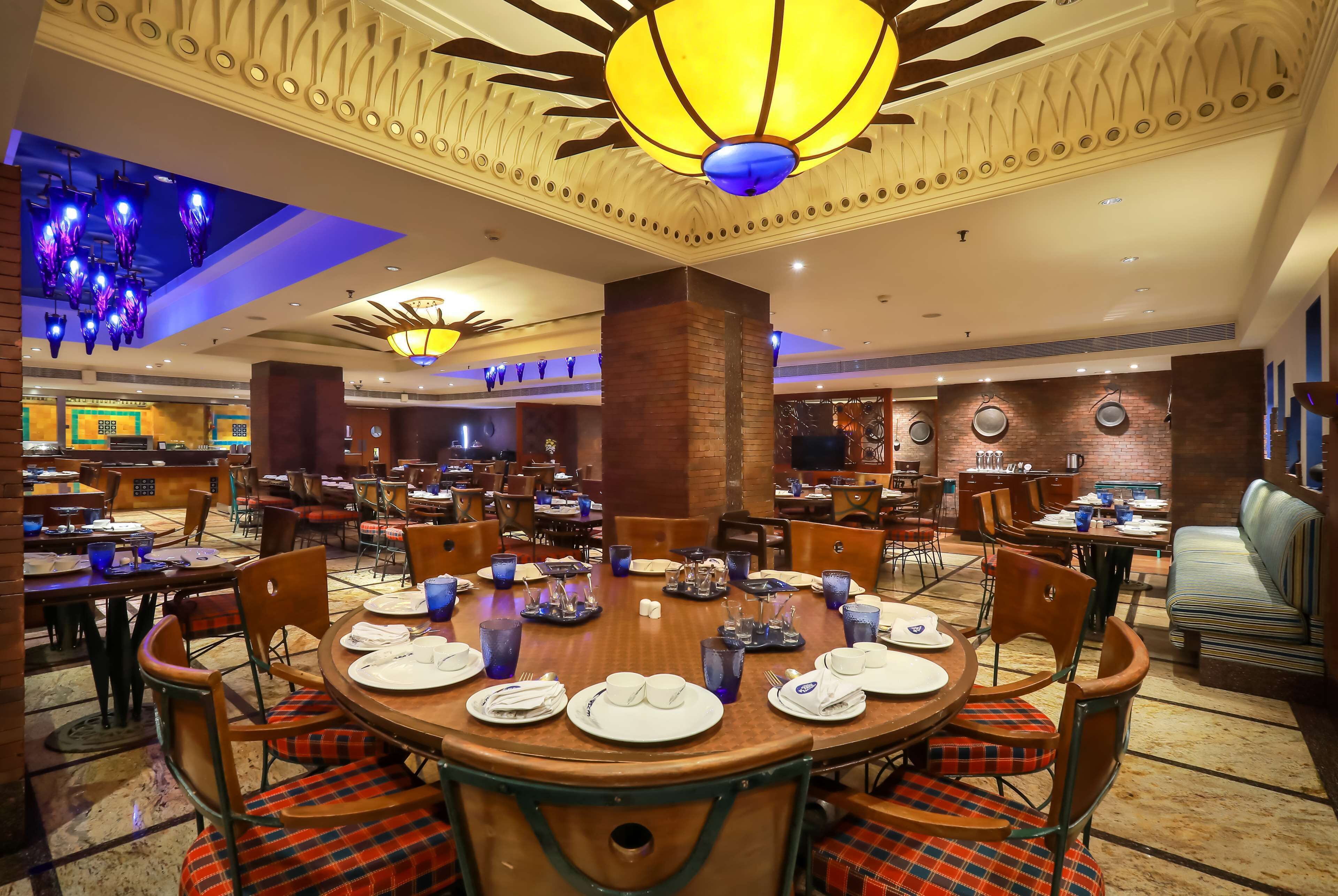Ein Hotelrestaurant mit runden Tischen für vier Personen, gedeckt mit Geschirr, Besteck und blauem Glas.