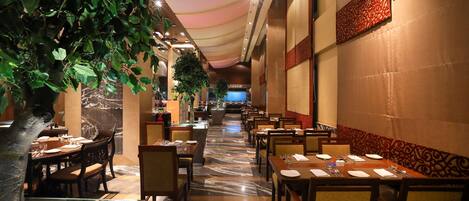 A restaurant with marble flooring, tables set with white tablecloths, and a ceiling with a draped fabric design.