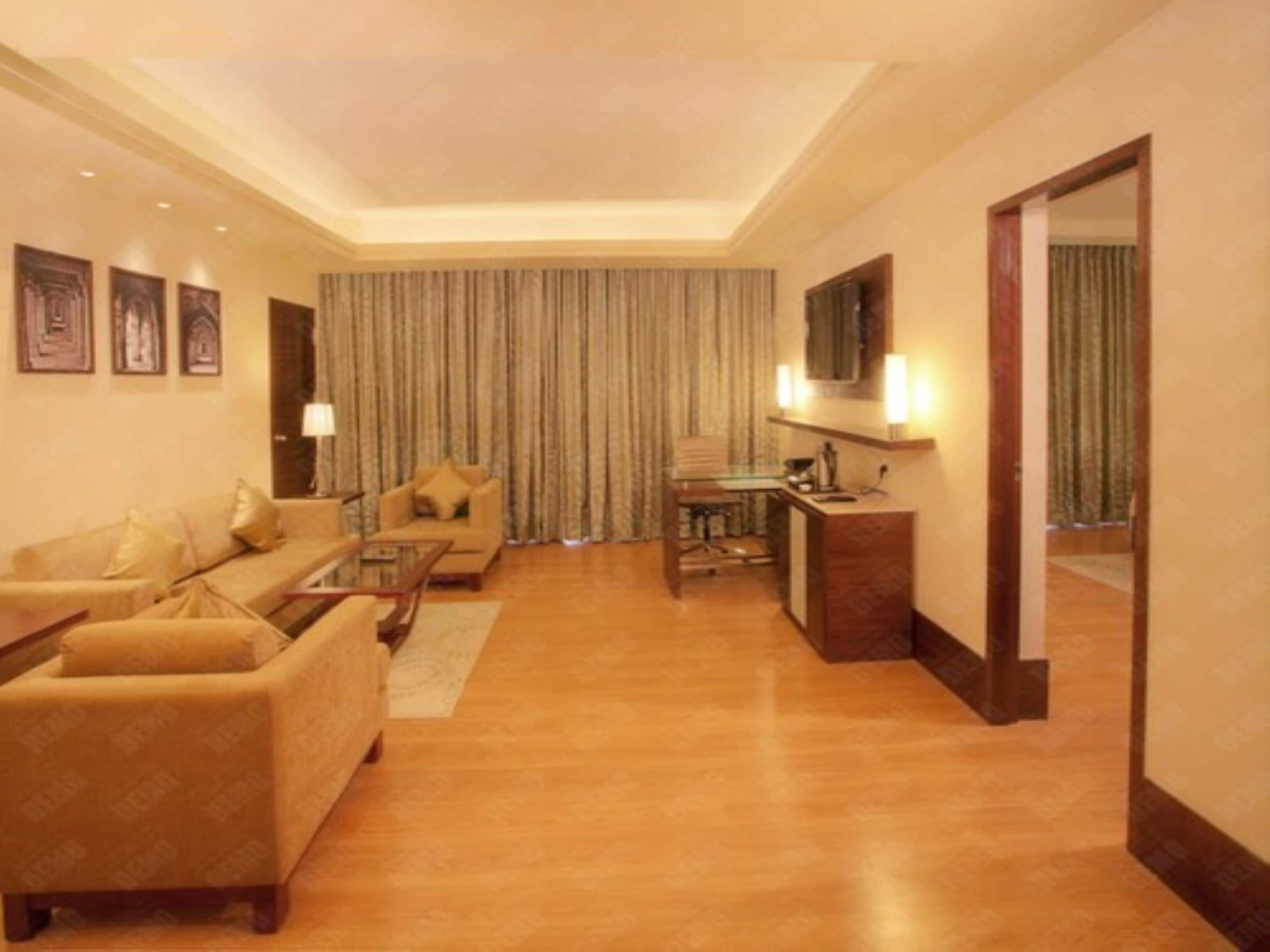 Quarto de hotel com sala de estar, incluindo um sofá, uma mesa de centro, uma escrivaninha com cadeira e uma televisão.