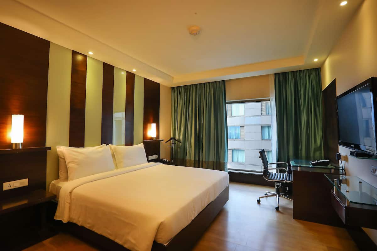 Ein Hotelzimmer mit einem großen Bett, einem Schreibtisch mit Stuhl, einem Fernseher und einem Fenster mit Vorhängen.