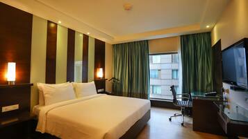Une chambre d’hôtel avec un grand lit, un bureau avec une chaise, une télévision et une fenêtre avec des rideaux.