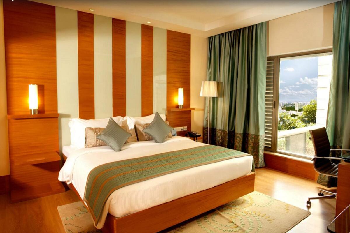 Ein modernes Hotelzimmer mit einem großen Bett, zwei Nachttischlampen, Blick auf die Stadt und einem Schreibtisch mit Stuhl.