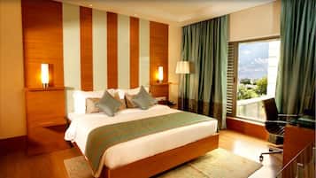 A modern hotel room with a large bed, two bedside lamps, a view of the city, and a desk with a chair.