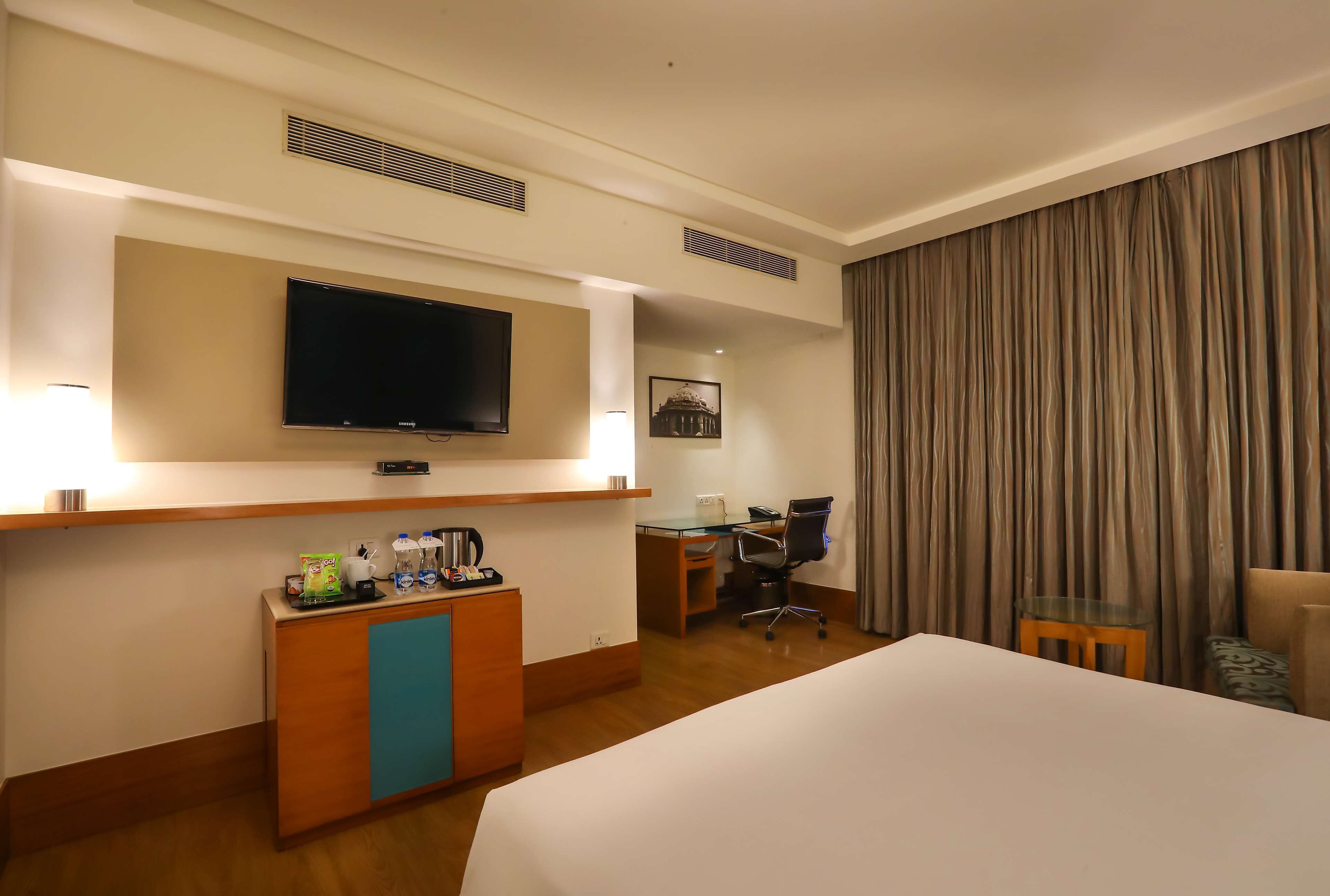 A hotel room with a bed, a desk, a chair, a television, a coffee station, and a curtain.