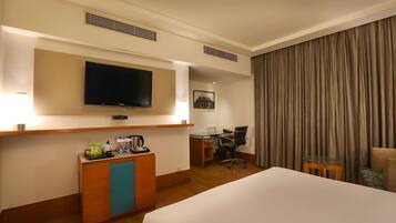 Habitación de hotel con cama, escritorio, silla, televisor, estación de café y cortina.