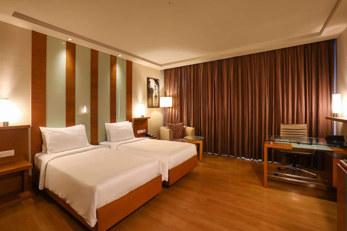 Ein Hotelzimmer mit zwei Betten, einem Schreibtisch, einem Stuhl, einer Lampe und einem Vorhang.