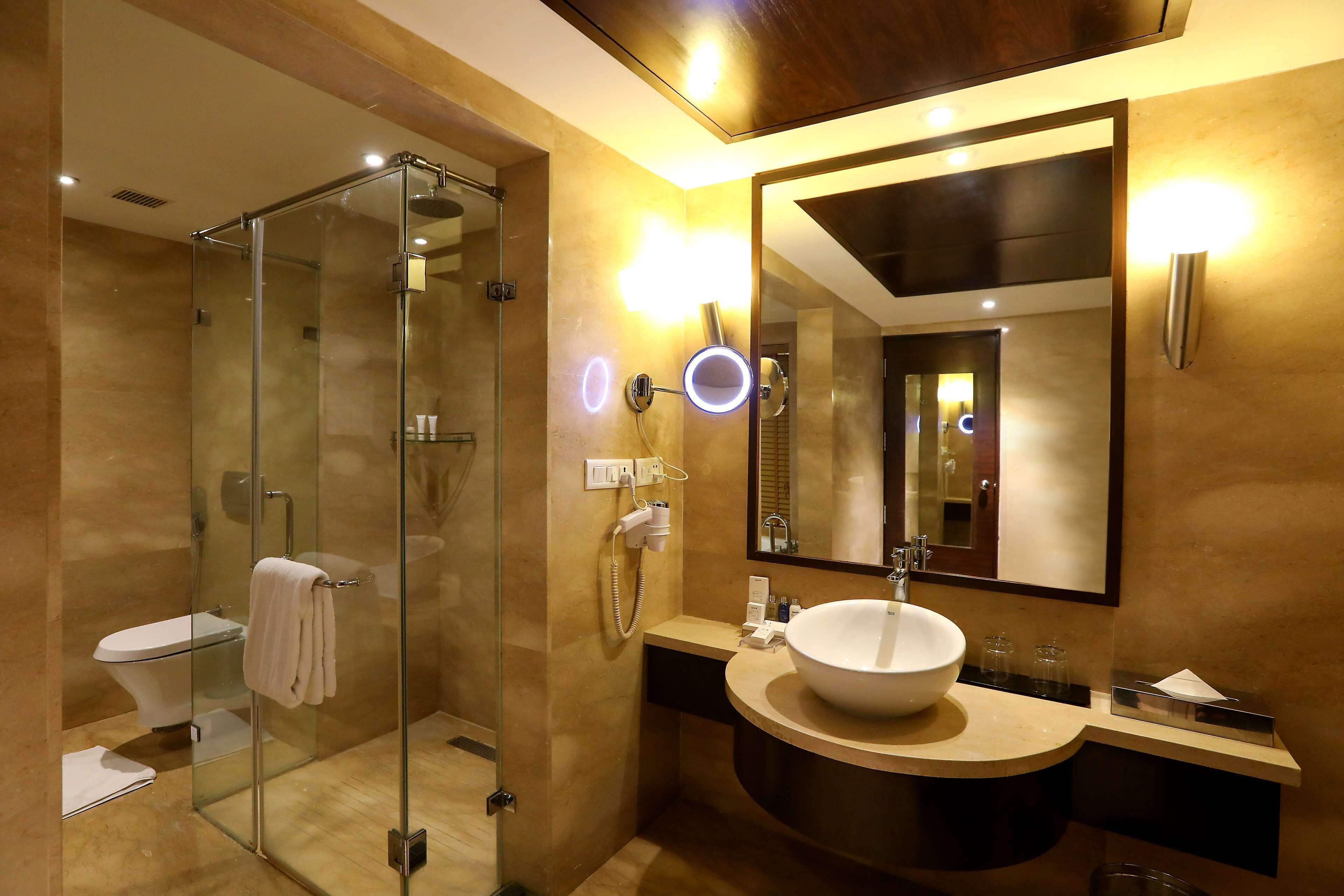 A modern bathroom with a glass-enclosed shower, a large vanity with a vessel sink, and a mirror with integrated lighting.