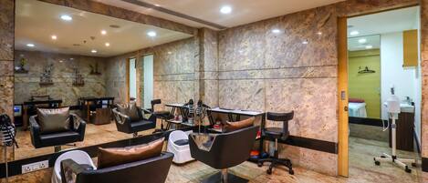 Un salón moderno con paredes de mármol, varias estaciones de peluquería y un espejo grande.