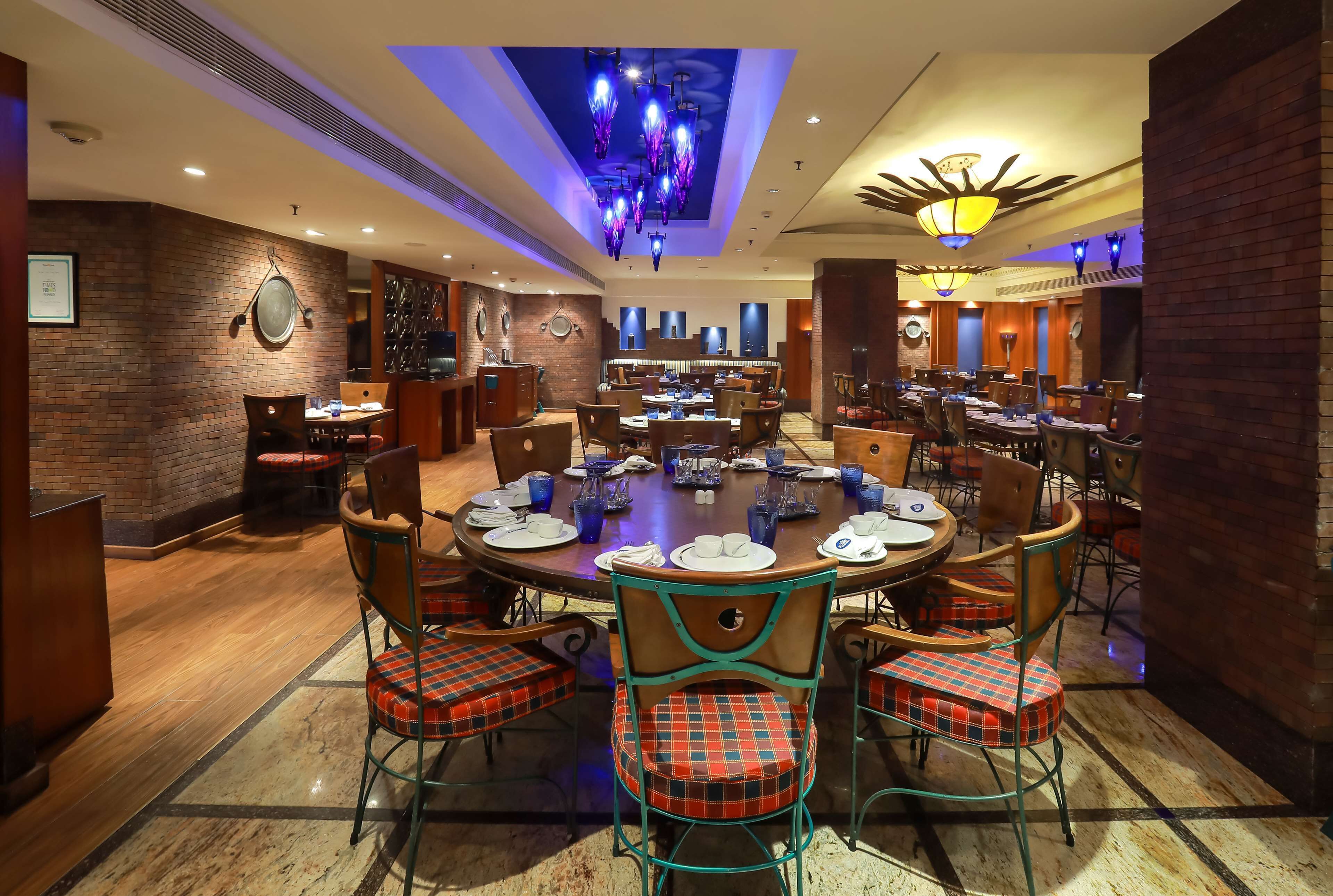 A restaurant with a central round table set for dining, surrounded by chairs with plaid cushions.
