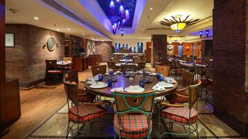 A restaurant with a central round table set for dining, surrounded by chairs with plaid cushions.