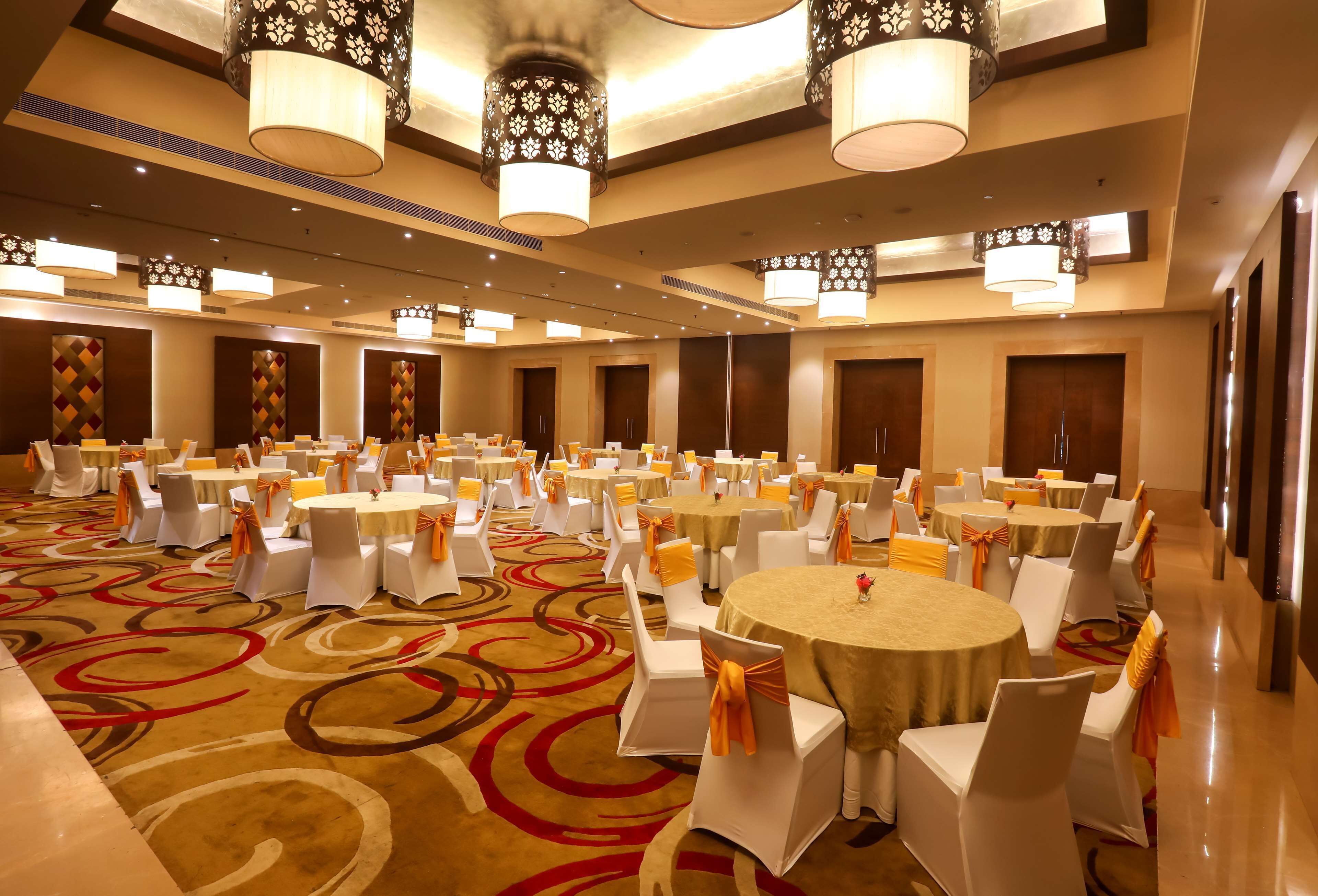 Un salón de banquetes con mesas redondas, sillas blancas y cintas anaranjadas.