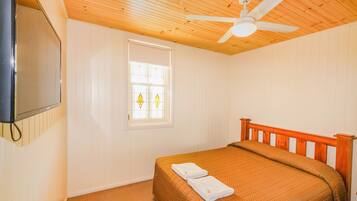 A bedroom with a wooden ceiling, a bed with a brown bedspread, a window with stained glass, and a ceiling fan.