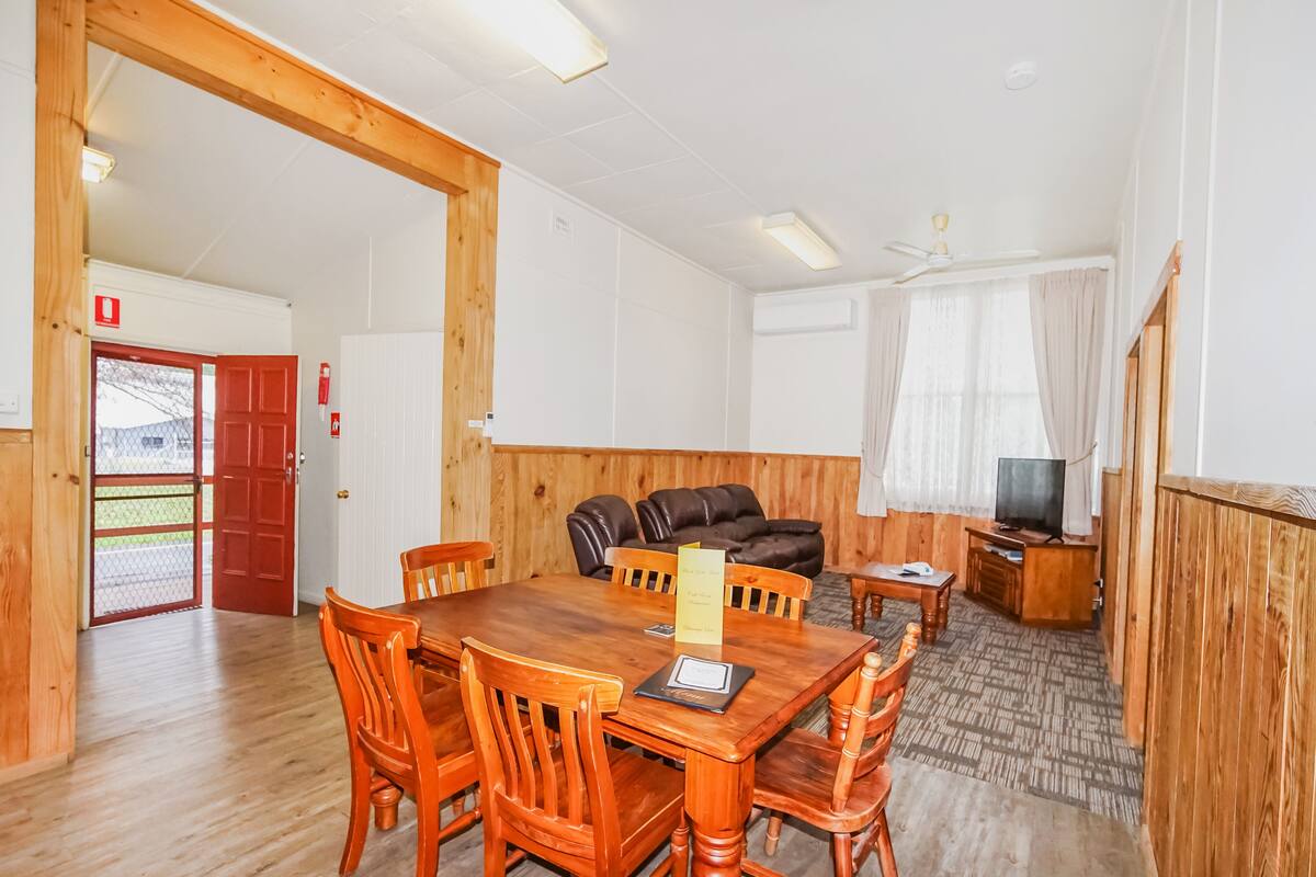 A room with a wooden dining table, chairs, a sofa, and a television.
