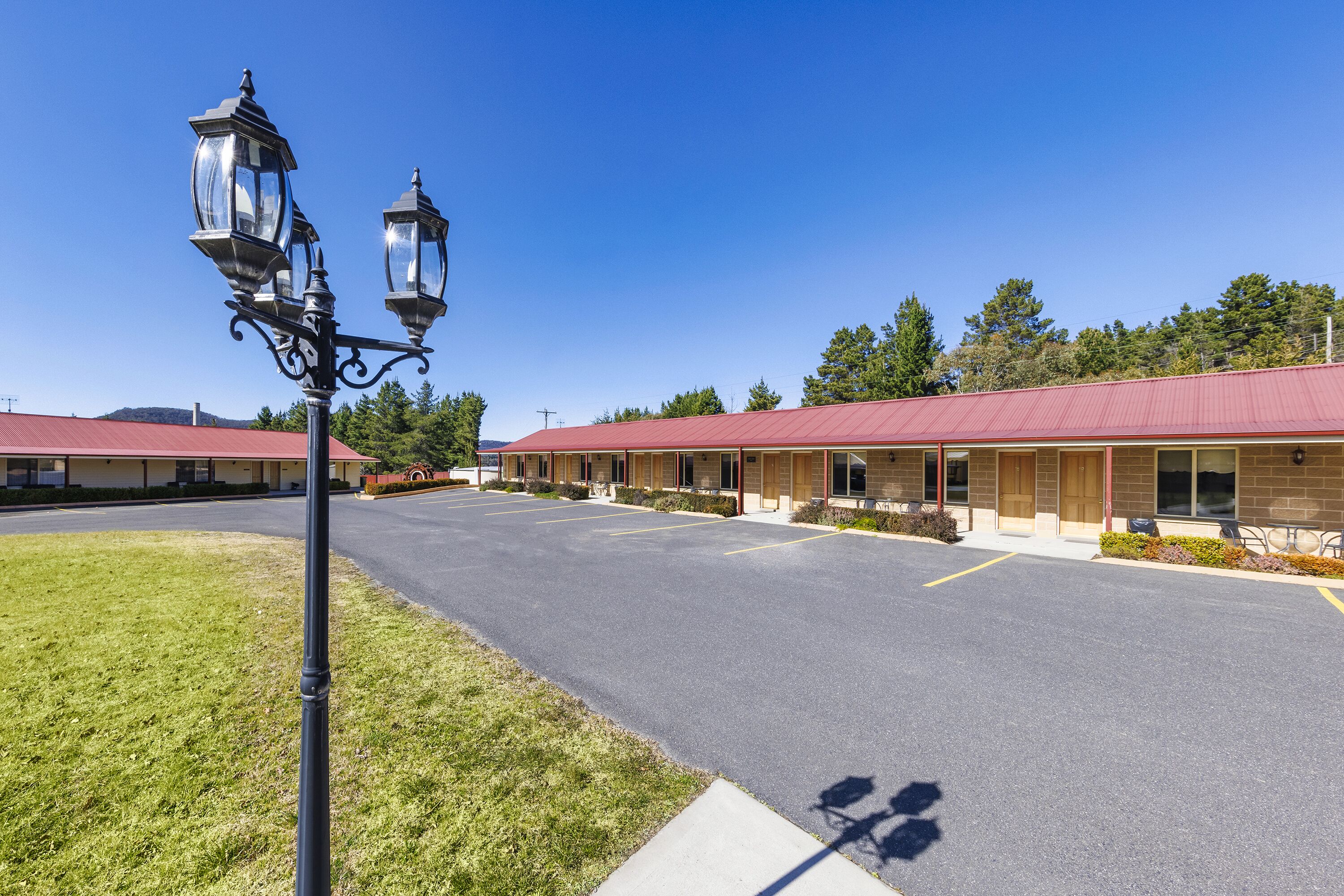 A motel with a red roof, a parking lot, and two street lamps.