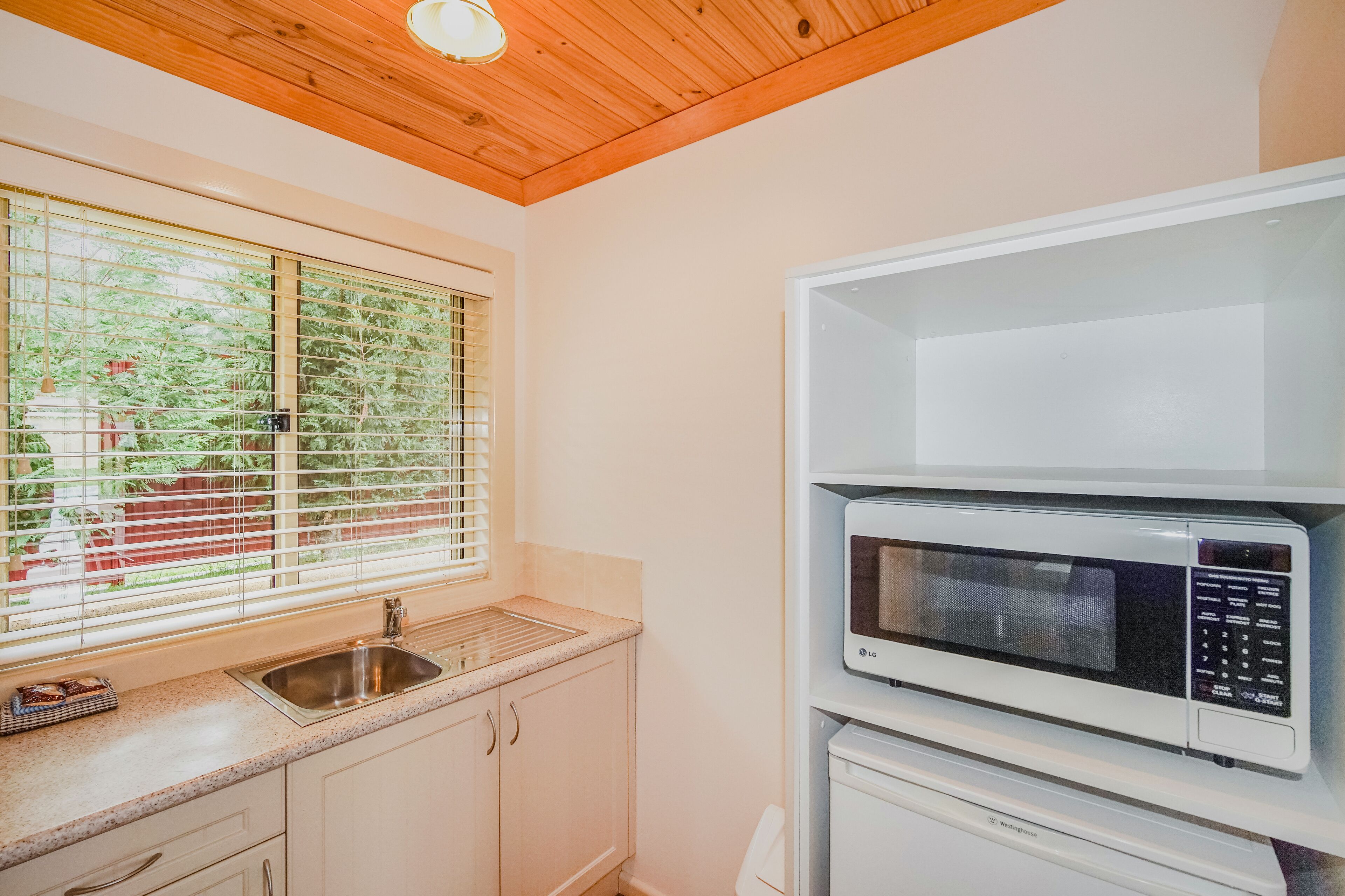 Una cocina con ventana, un lavamanos y un microondas.