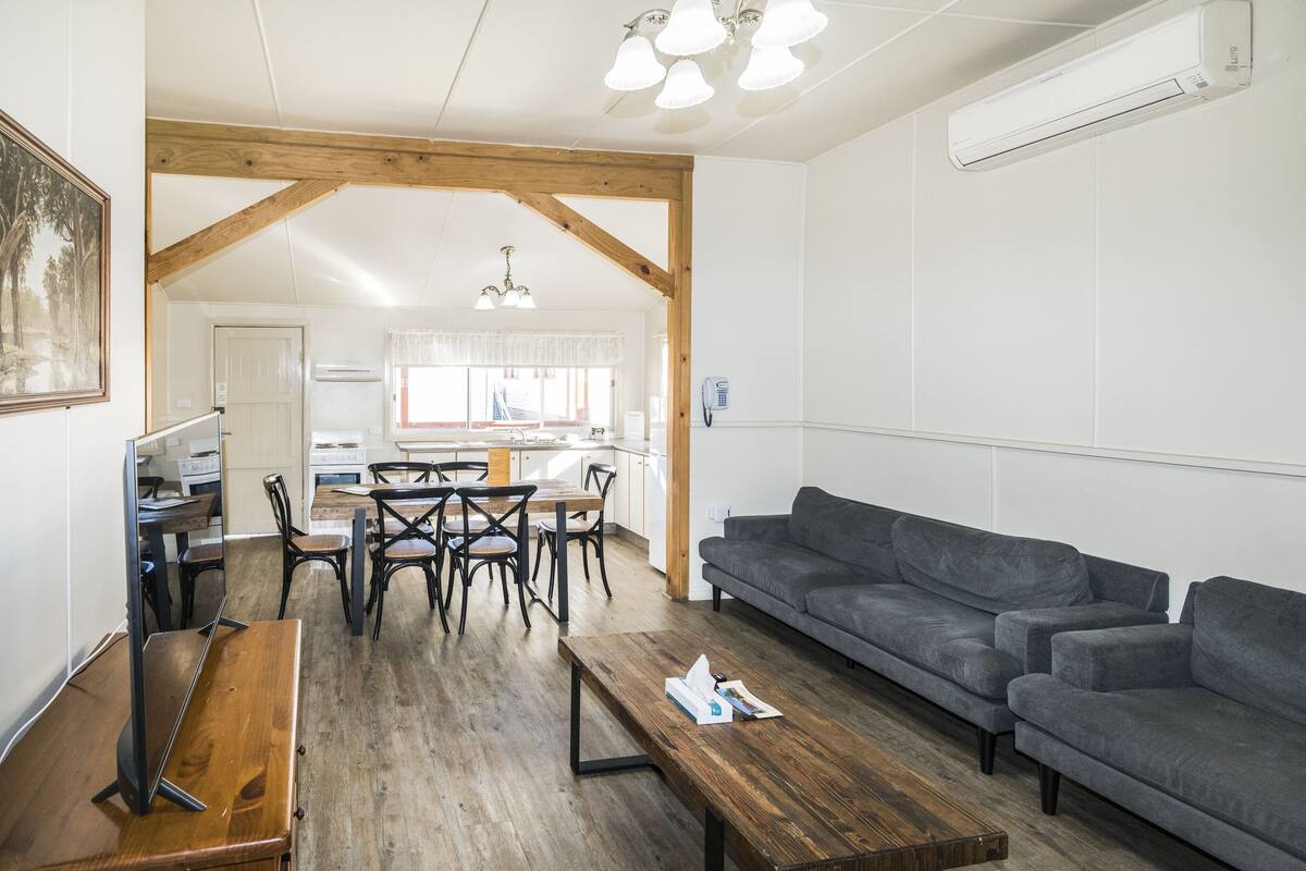 A spacious living area with a wooden floor, a gray sofa, a wooden coffee table, and a dining area with chairs and a table.