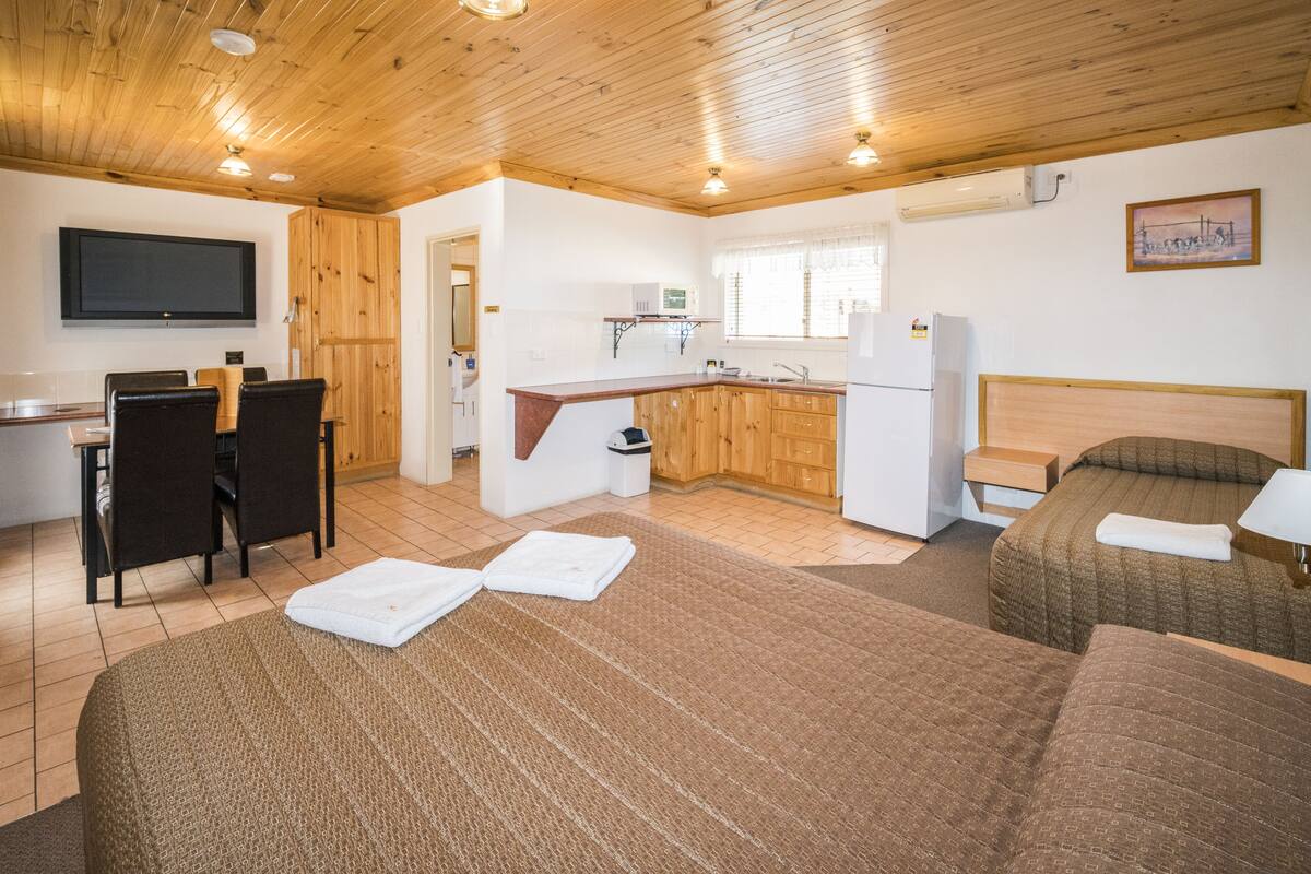 A compact hotel room with a kitchenette, a dining area, and two beds.