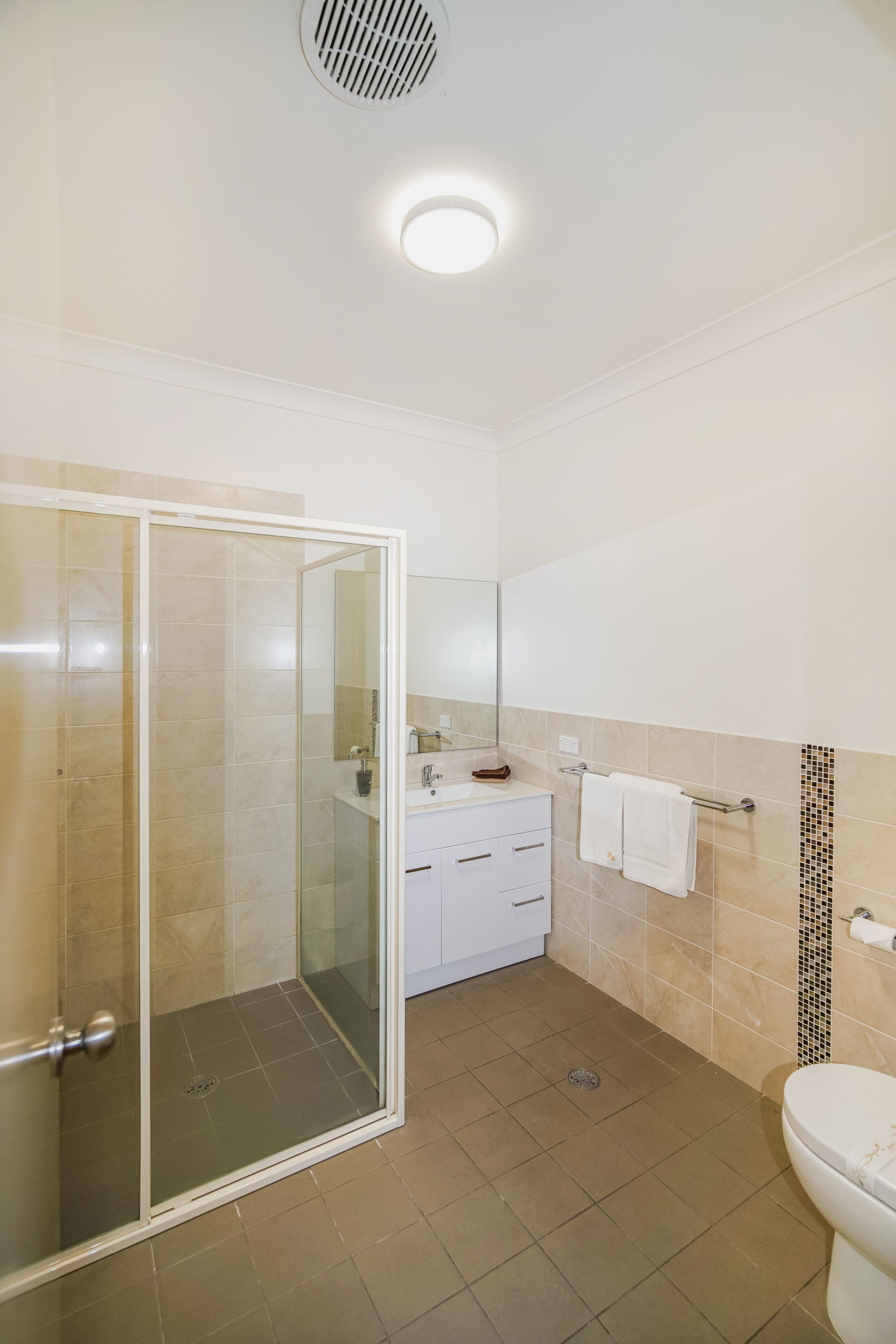 A bathroom with a glass shower enclosure, a toilet, a sink with a mirror, and a towel rack.