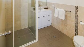 A bathroom with a glass shower enclosure, a toilet, a sink with a mirror, and a towel rack.