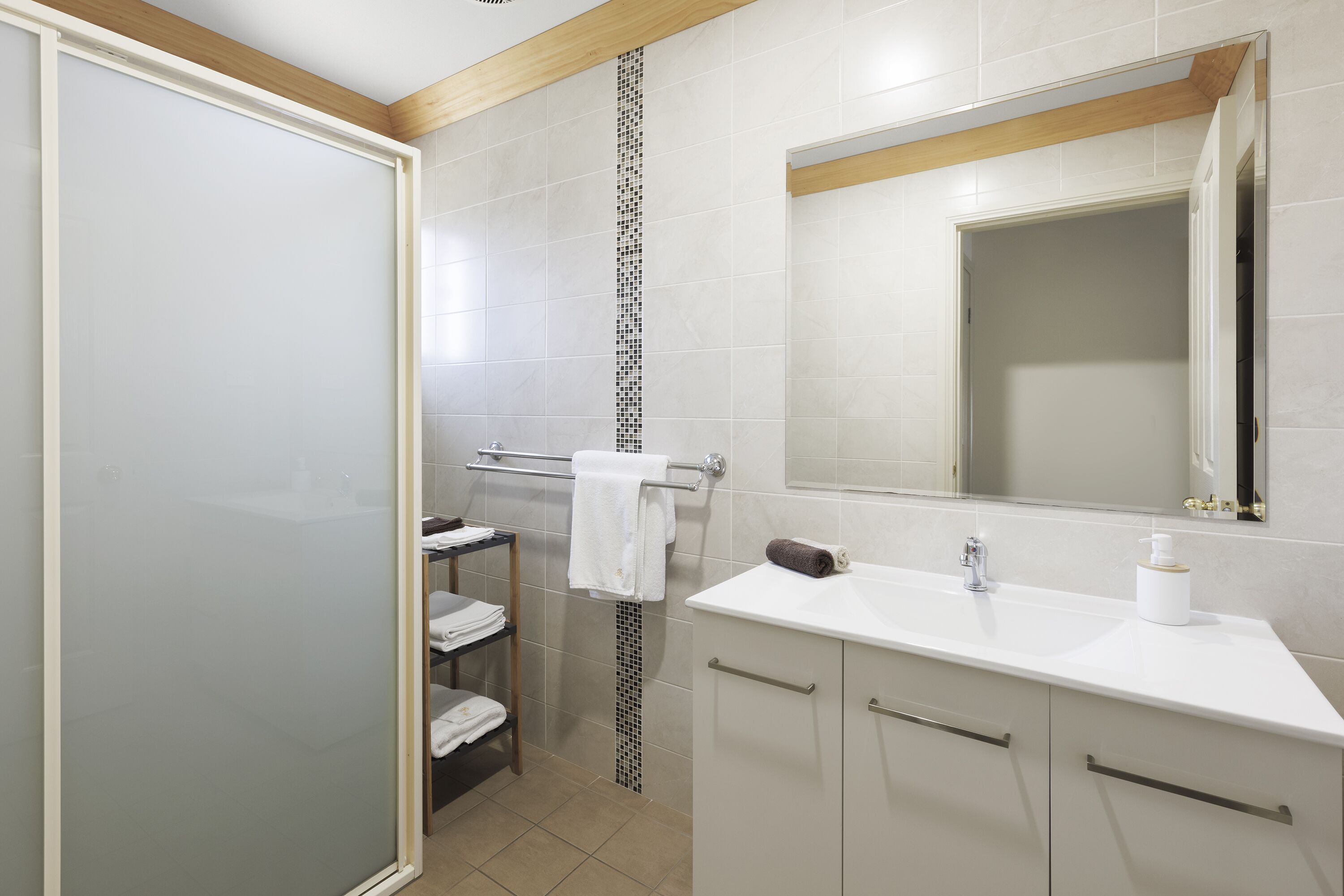 A modern bathroom with a glass shower enclosure, a white sink with a mirror above, and a towel rack with folded towels.