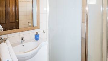 A bathroom with a white sink, a mirror, a glass shower enclosure, and a wooden ceiling.
