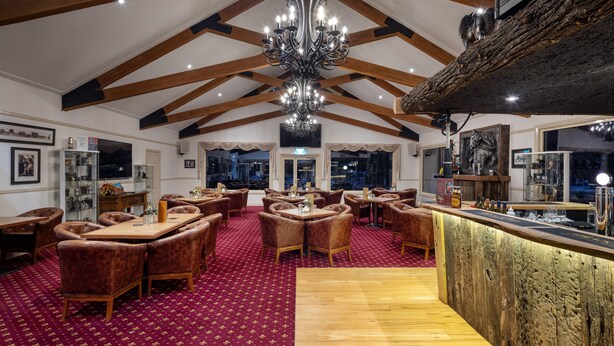 Um quarto espaçoso com tetos altos, vigas de madeira e um candelabro. Várias mesas e cadeiras dispostas para refeições.