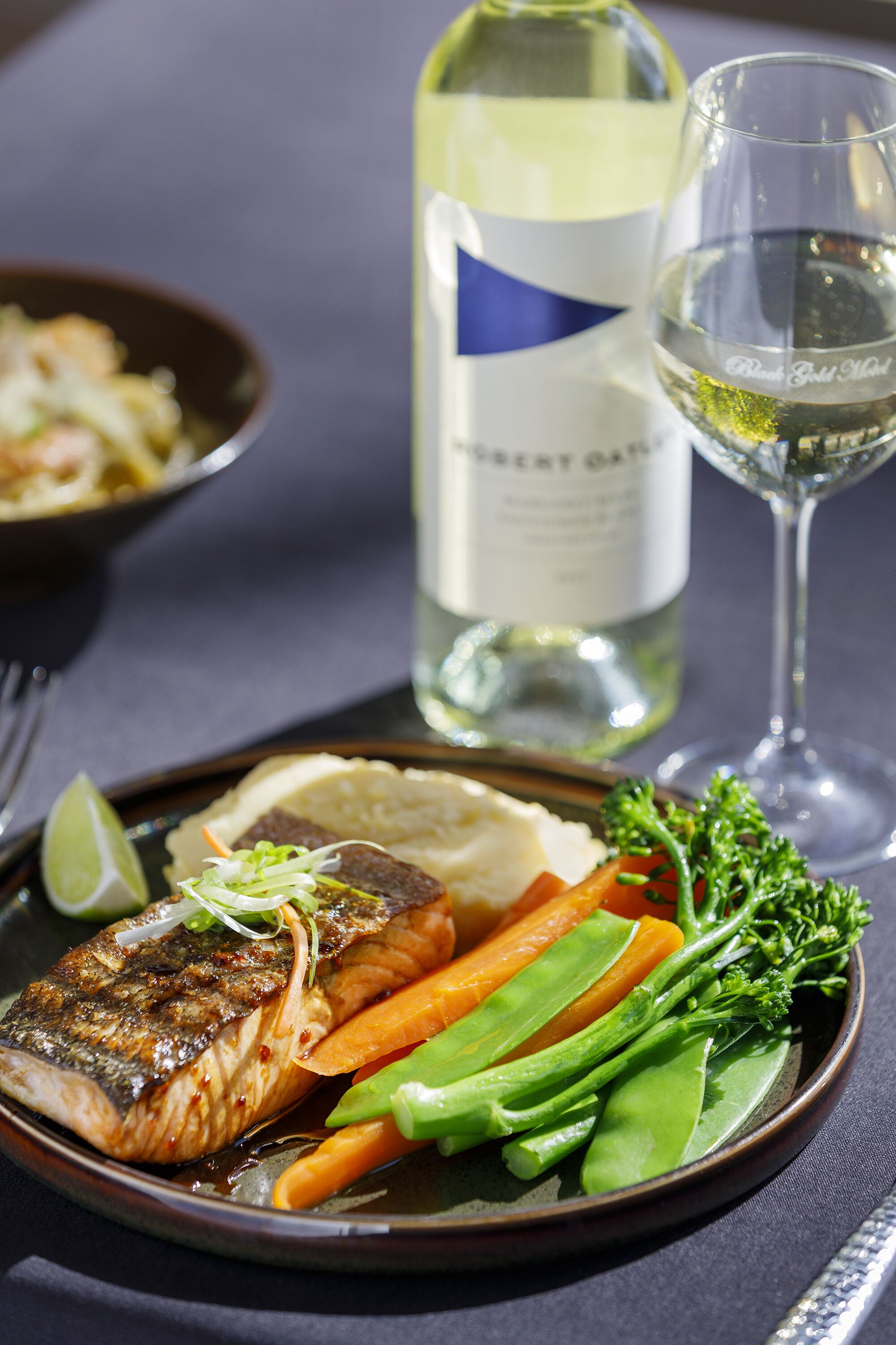 A plate of grilled fish with vegetables and a glass of white wine on a table.