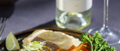 A plate of grilled fish with vegetables and a glass of white wine on a table.