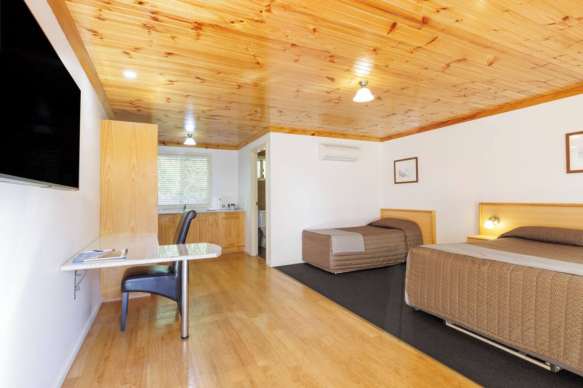 A room with a wooden ceiling, a bed, a desk, and a chair.